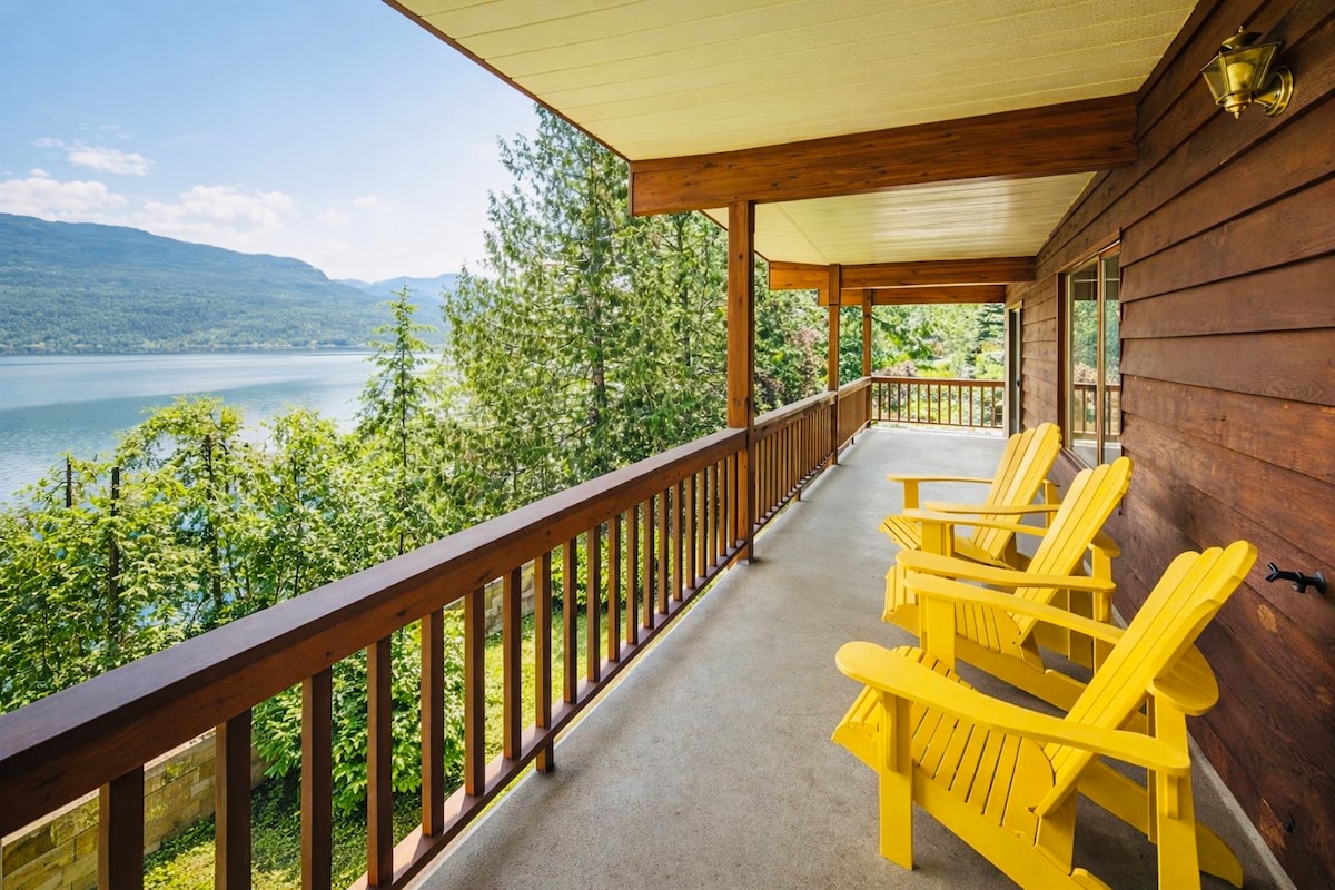 Covered lakeside deck with yellow Adirondack chairs overlooking Kootenay Lake and the mountains