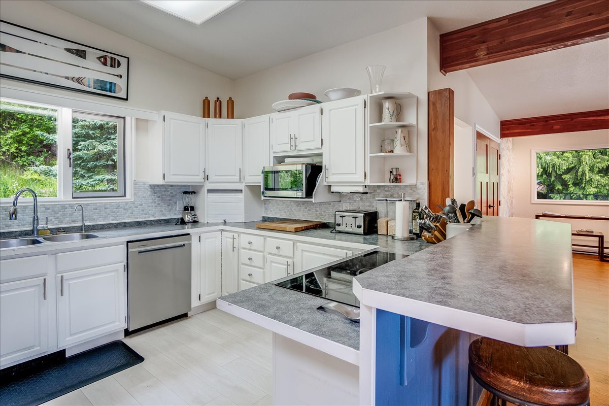Fully equipped kitchen with white cabinetry, granite island, induction stovetop, dishwasher, and stainless appliances