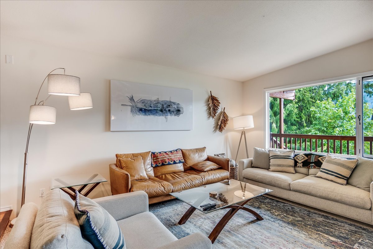 Main floor living room with three couches around a glass coffee table and deck view through the window